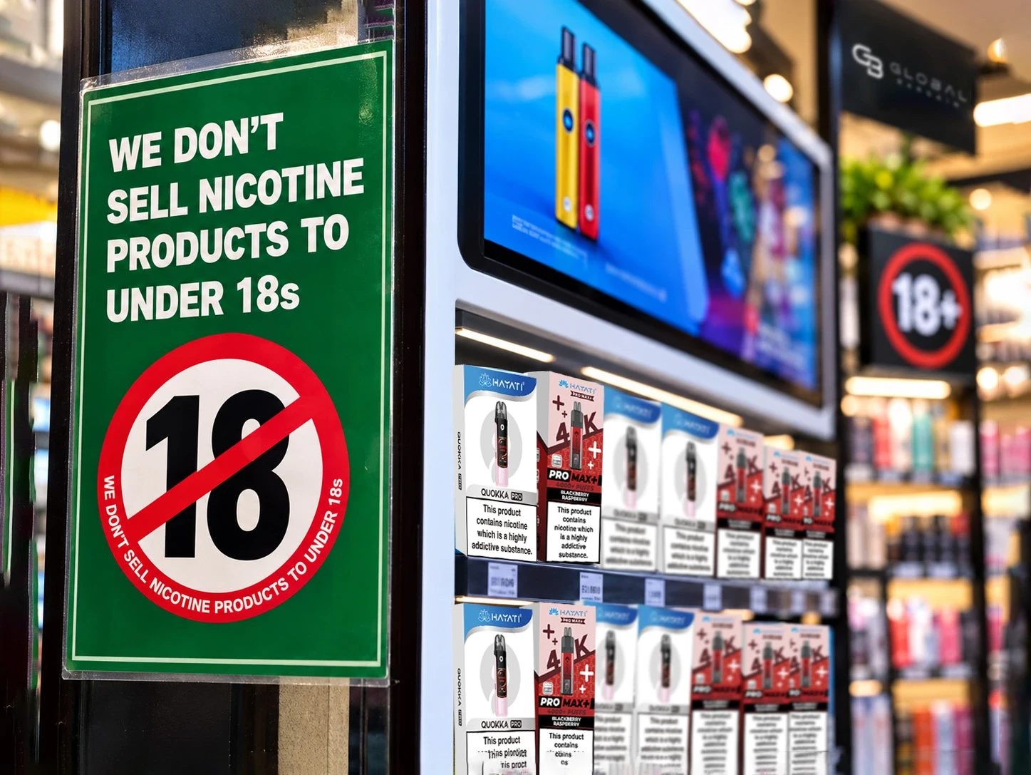 Retail vape display with a green “We don’t sell nicotine products to under 18s” sign beside Hayati vape shelves in a UK shop